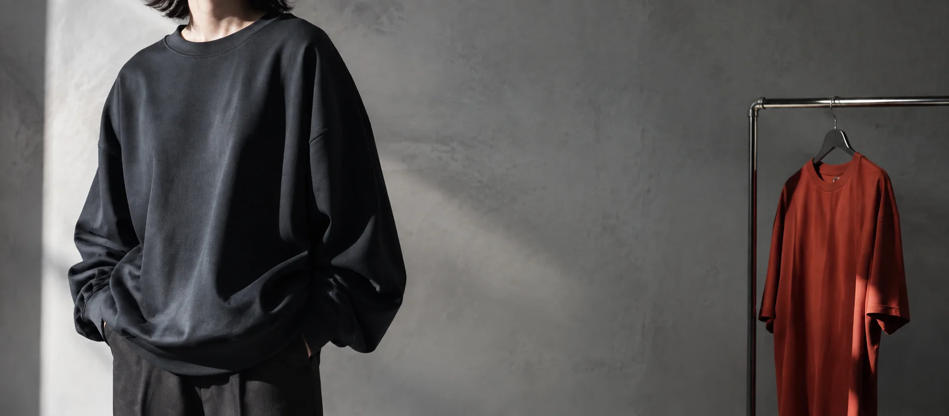 黒いスウェットを着た人物と、ラックに掛けられた赤いTシャツ
